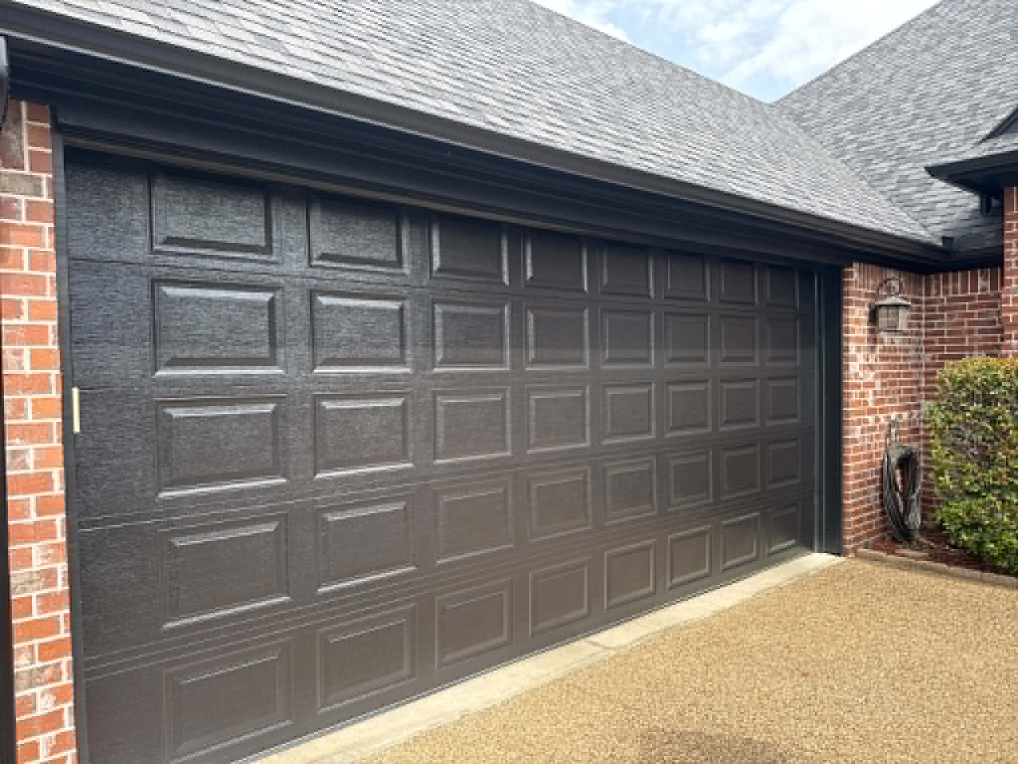 A new black garage door installed on a red-brick East Texas home